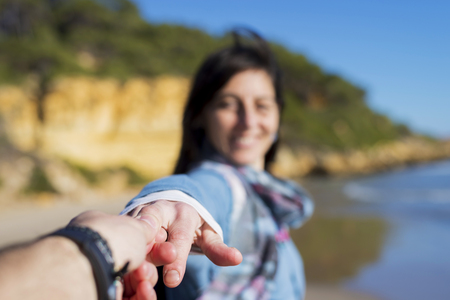 Couple having fun with woman taking man by the hand and pulling towards the sea, enjoying a summer holiday together on a beach. Fun travel and lifestyle romantic vacation, nature exteriorの写真素材