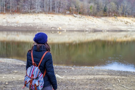 Hiking woman with backpack standing by the lake.
