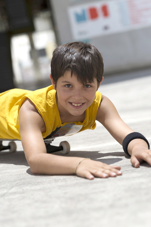 Young smiling boy on a skateboard while looking camera on a sunny dayの写真素材