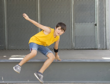 Front view of a smiling boy jumping over a metallic fence while looking camera on a bright dayの写真素材