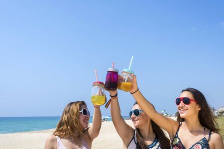friendship and leisure concept - group of happy young women or female friends toasting non alcoholic drinks on summer beachの写真素材