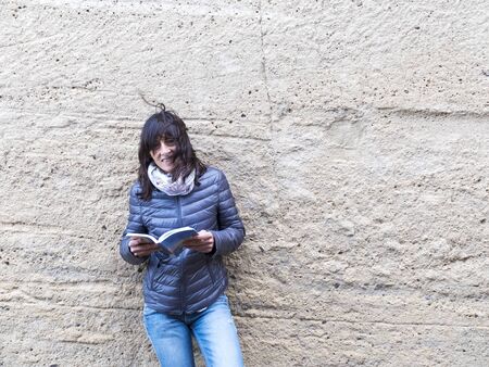 Woman standing against wall holding a travel guide while looking camera