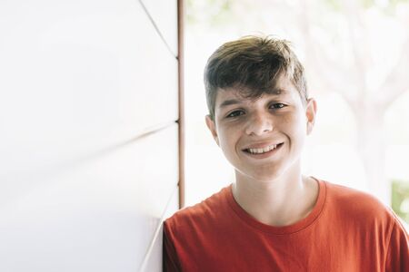 Portrait of a cheerful male teen leaning on wood wall while looking camera in a sunny dayの写真素材