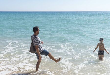 Father and son playing with water on seashoreの写真素材