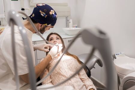Young bearded dentist drilling tooth to female patient.の写真素材
