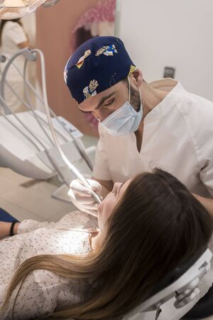 Young bearded dentist drilling tooth to female patient.の写真素材