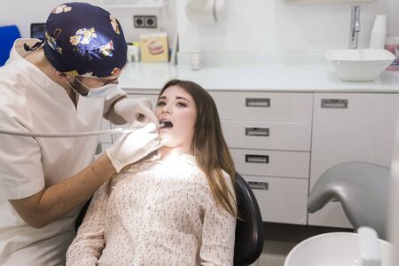 Young bearded dentist drilling tooth to female patient.