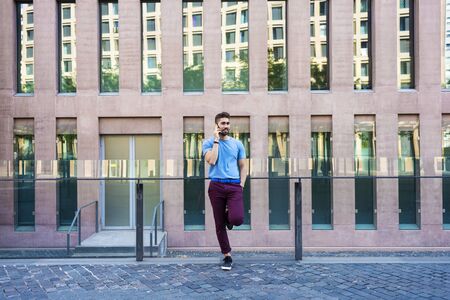 Portrait of cheerful modern businessman speaking by phone and smiling while standing outdoorsの写真素材