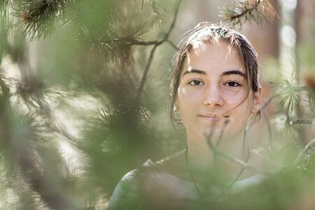 Young girl in T-shirt standing hiding into foliageの写真素材