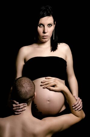 Male hugging a pregnant woman's belly while looking at the cameraの写真素材