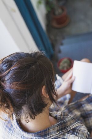 Above view of a young woman sitting on home staircase while reading a bookの写真素材