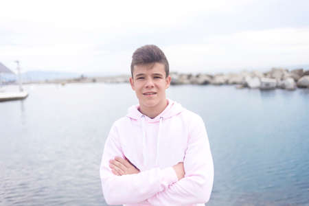 Young teenager with crossing arms standing on promenade while looking at camera