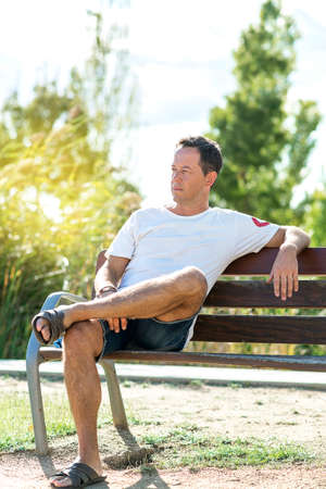 Handsome man in white t-shirt standing in a city park while looking at cameraの写真素材