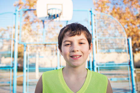 Young teen male with sleeveless standing on a street basket court while smiling at camera