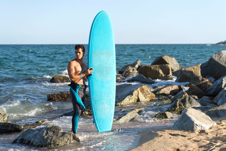 handsome and attractive surfer man in neoprene swimsuit holding surf board posing cool after surfing enjoying Summer water sport and holidaysの写真素材