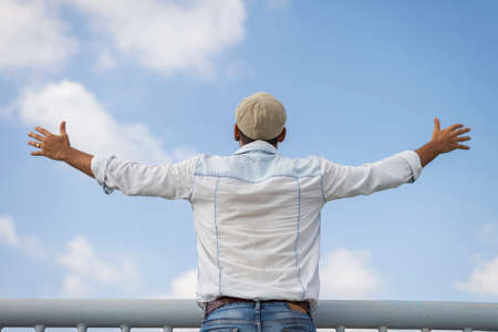 Back view of a man raising his arms up against sky
