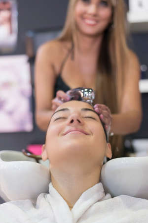 Front view of a hairdresser washing hair of a beautiful young lady in hair salon.の写真素材