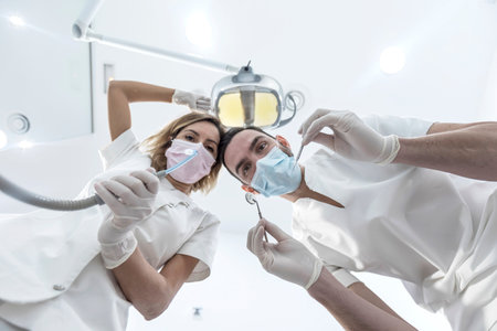 Man and woman two dentists in medical face masks and rubber gloves doing treatment, low angle shot...