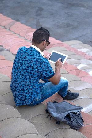 A Rear image of young man sitting on bleachers using a tabletの写真素材