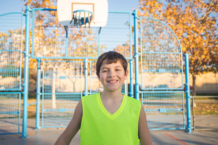 Half-length portrait of a smiling boy in a tank top smiling at the camera on an urban basketball court at dusk.の写真素材