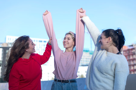 Three joyful friends outdoors, hands raised high in a show of unity and happiness, with one in a red...