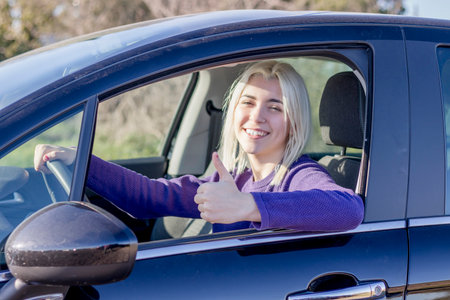 A smiling woman in a car giving a thumbs up, possibly indicating a good driving experience or...