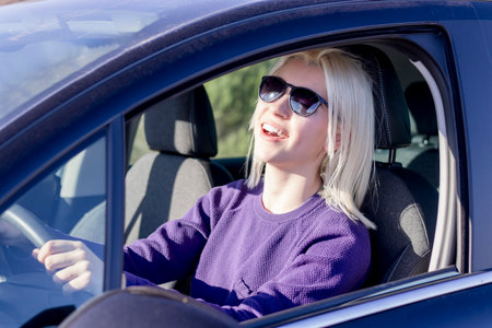 A joyful blonde woman with sunglasses driving a car, laughing and looking cheerful, exemplifying the...