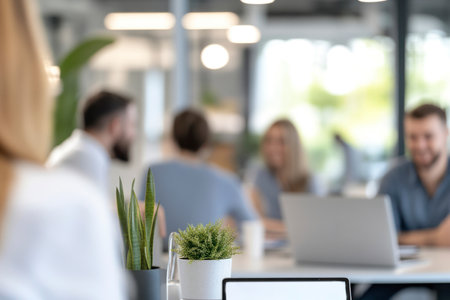 A contemporary office setting with potted plants in focus while blurred employees collaborate in the background. Bright, modern, and professional workspace.の素材