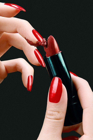 hands of a young woman with red polish nails grating red lipstickの写真素材