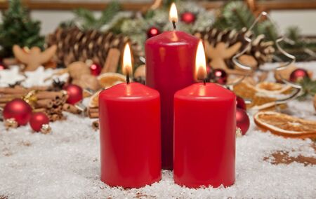 A glowing red candle with christmas decorations の写真素材