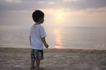 Portrait of a little boy standing looking at the vast sea. A picture of a little boy standing to look at the vast sea and the sunset. Copy space for caption on right side.の写真素材