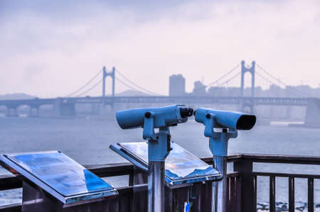 Coin-operated binoculars. Binocular telescope on the observation deck for tourism. Spyglass or telescope pointing towards the sea, city background. A telescope on the other side of the river.の写真素材