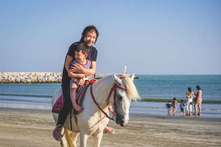 Mom and her son are riding a white horse on the beach. The family spends time with their children...