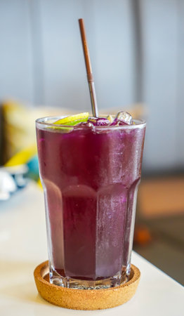 Purple juice in a glass with ice and straw on the tableの写真素材