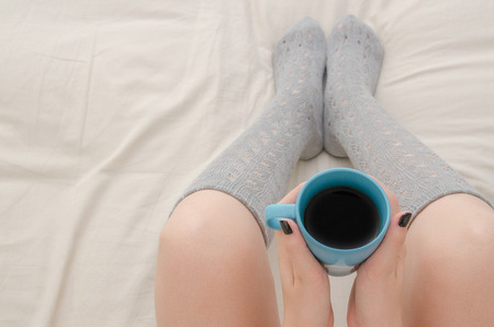 Woman sitting on bed with gray socks and cup of coffeeの写真素材