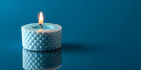 Serene blue candle glows with warm light, reflecting on a smooth, dark surfaceの写真素材