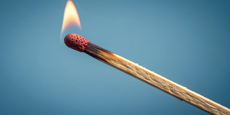 Burning match ignites with vibrant flame against blue background, symbolizing ideas and conceptsの写真素材