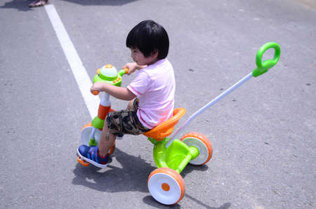 Active asian kid boy driving tricycle or bicycle at road. Toddler child having fun on warm summer...