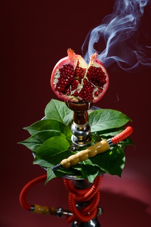 Smoking hookah with fruit head on dark background