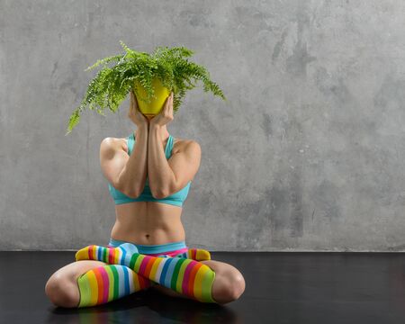 Woman in colored clothes meditates in yoga pose with plantの写真素材
