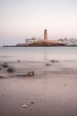 Sunrise on a rocky beach with a lighthouse in the background at Sur's bay, Omanの写真素材