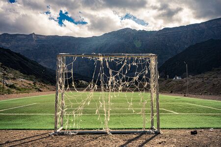 Rear view of a soccer goal with broken nets on a soccer field between mountains in Jebel Shams, Omanの写真素材