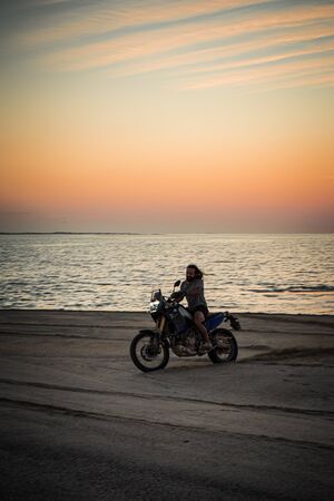 Masirah Island, Oman, January 1, 2020: Man on a motorcycle on the beach at sunsetの写真素材