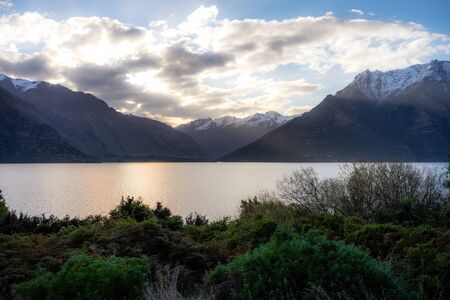 Gorgeous image of the snow capped mountains at the Wakatipu lake taken during an orange sunset in Queenstown, New Zealandの写真素材