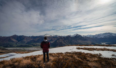Mount Aspiring, New Zealand, October 6, 2019: Stunning photograph of a European man admiring the snow capped mountains from the mountain across the river taken on a sunny dayのeditorial素材