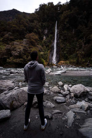 Haast Pass, New Zealand, October 6, 2019: Stunning photograph of a European man watching the water fall from Thunder Creek Fallsのeditorial素材
