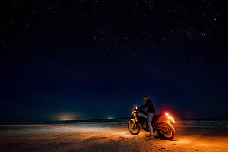 Masirah island, Oman, January 1, 2020: Gorgeous night image of a European man on a motorcycle with his lights on
in the middle of the desertの写真素材