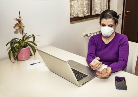 Corona Virus, Covid-19. Stay at home. Quarantine. Protection mask. A Caucasian woman forced to stay home to prevent virus infection, works on the laptop. Smart Working. Disinfect hands with gel.の写真素材