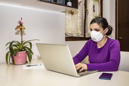 Corona Virus, Covid-19. Stay at home. Quarantine. Protection mask. A beautiful Caucasian woman forced to stay home to prevent virus infection, works on the laptop. Smart Working.の写真素材