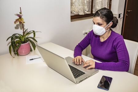 Corona Virus, Covid-19. Stay at home. Quarantine. Protection mask. A beautiful Caucasian woman forced to stay home to prevent virus infection, works on the laptop. Smart Working.の写真素材